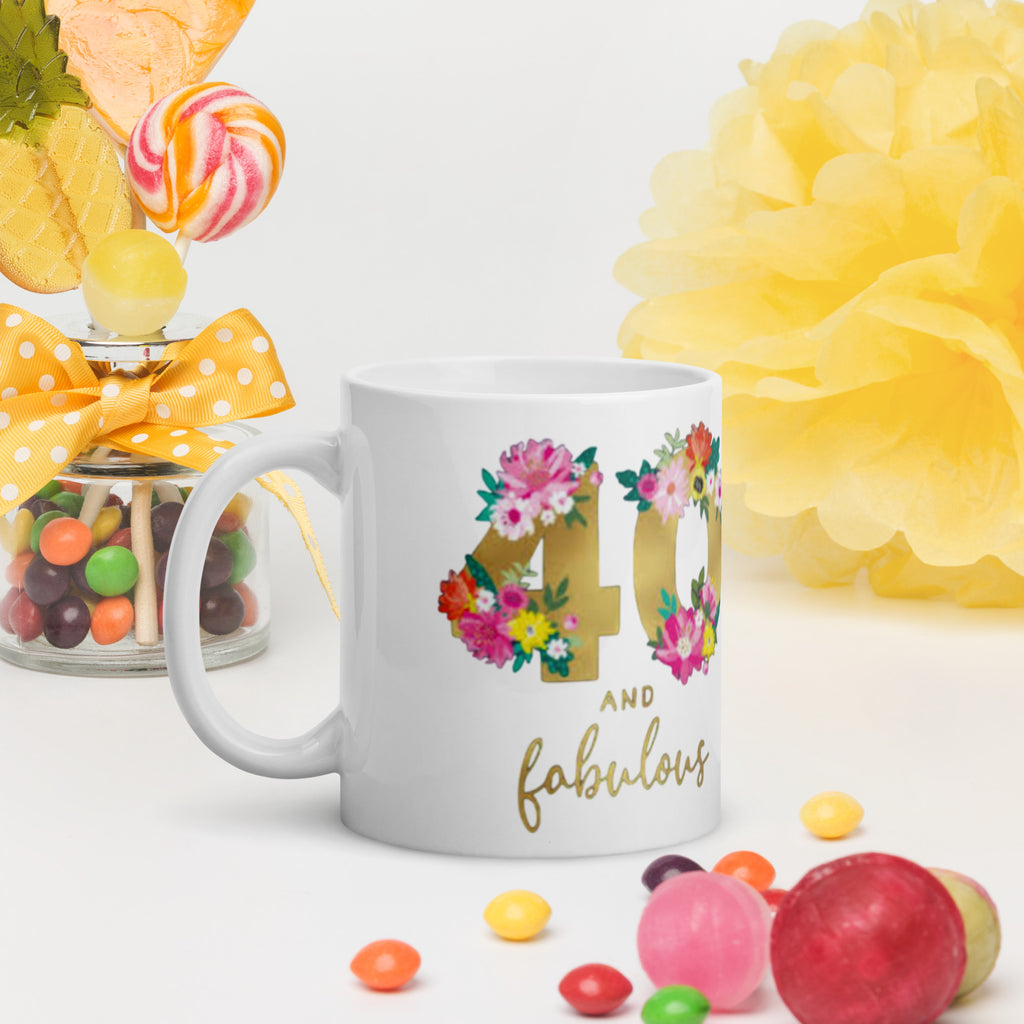 White mug with floral design and text, surrounded by colorful candies and flowers on a light background