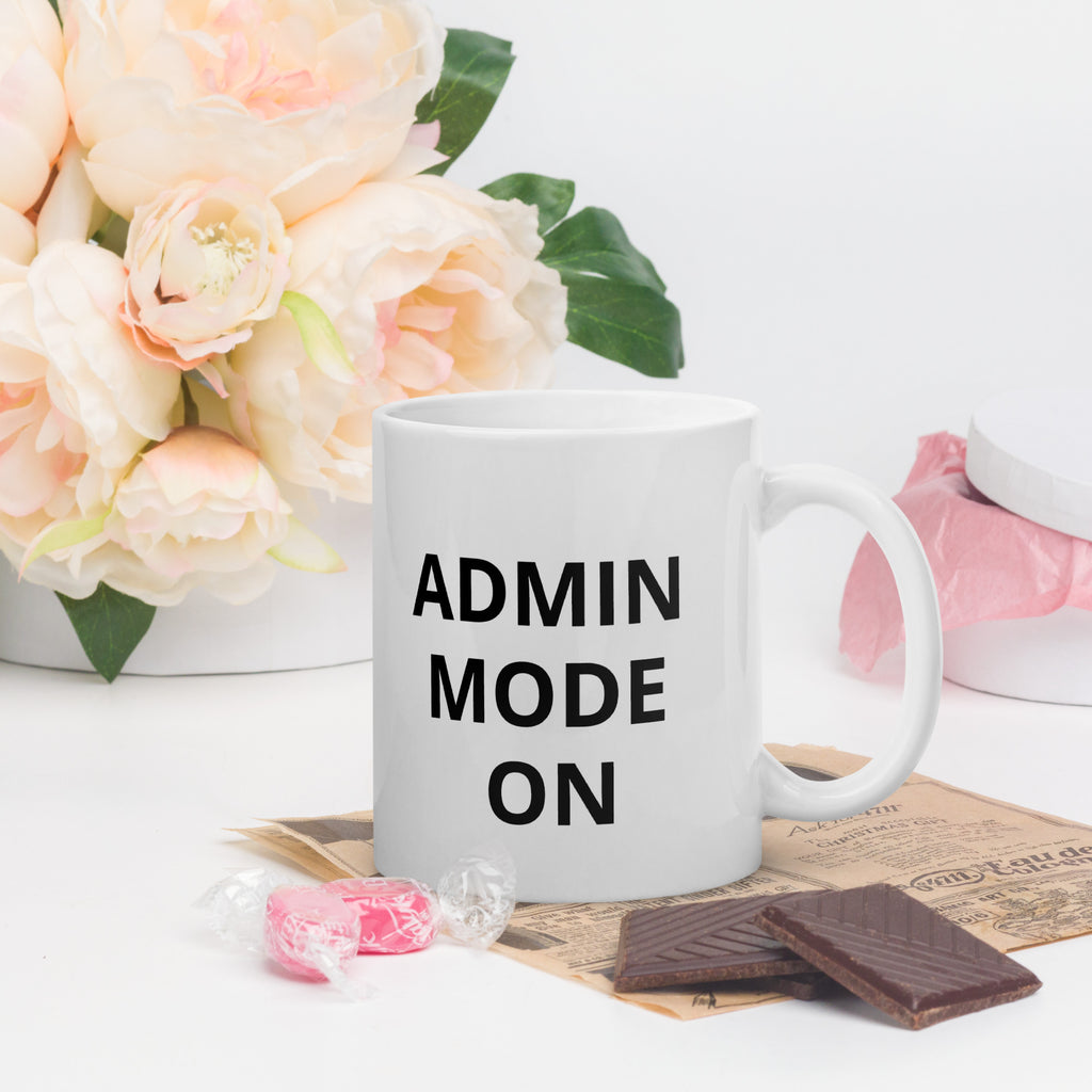 White mug with 'ADMIN MODE ON' text, flowers, and chocolate on a white background