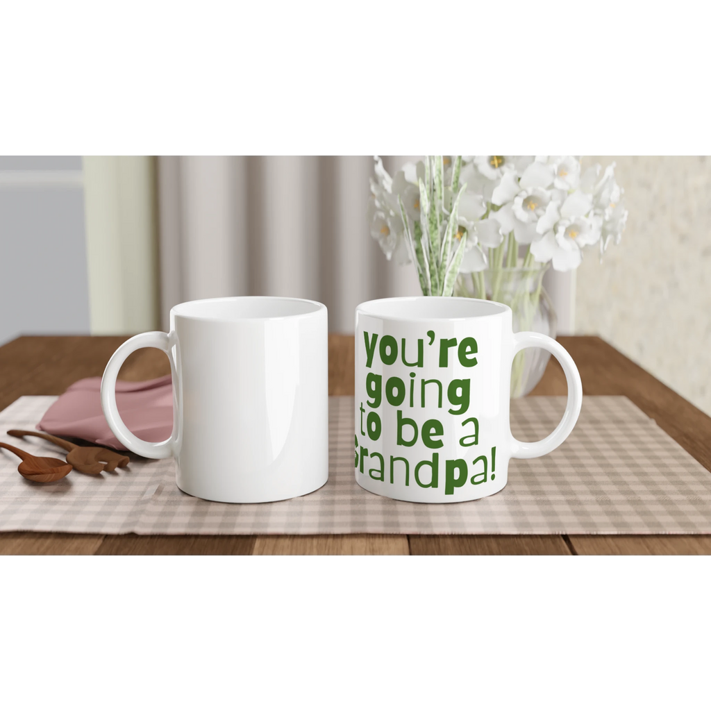 Two white mugs on a table with one displaying 'You're going to be a grandpa!' text.