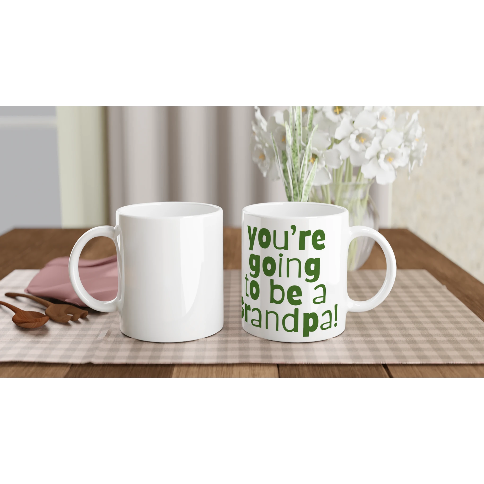 Two white mugs on a table with one displaying 'You're going to be a grandpa!' text.