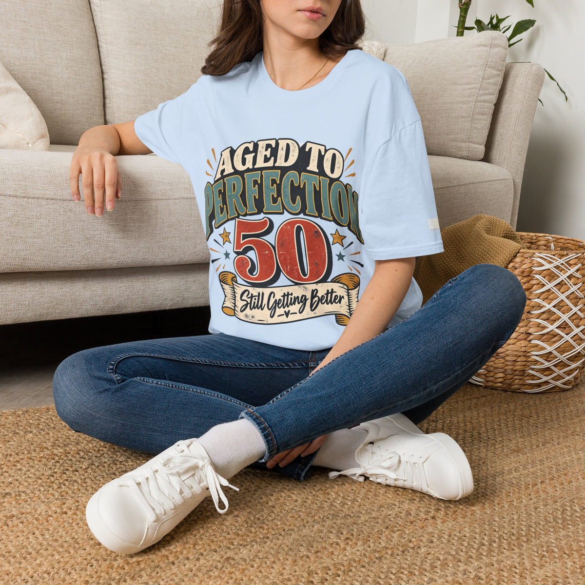 Person wearing a light blue t-shirt with 50 birthday design sitting on the floor.