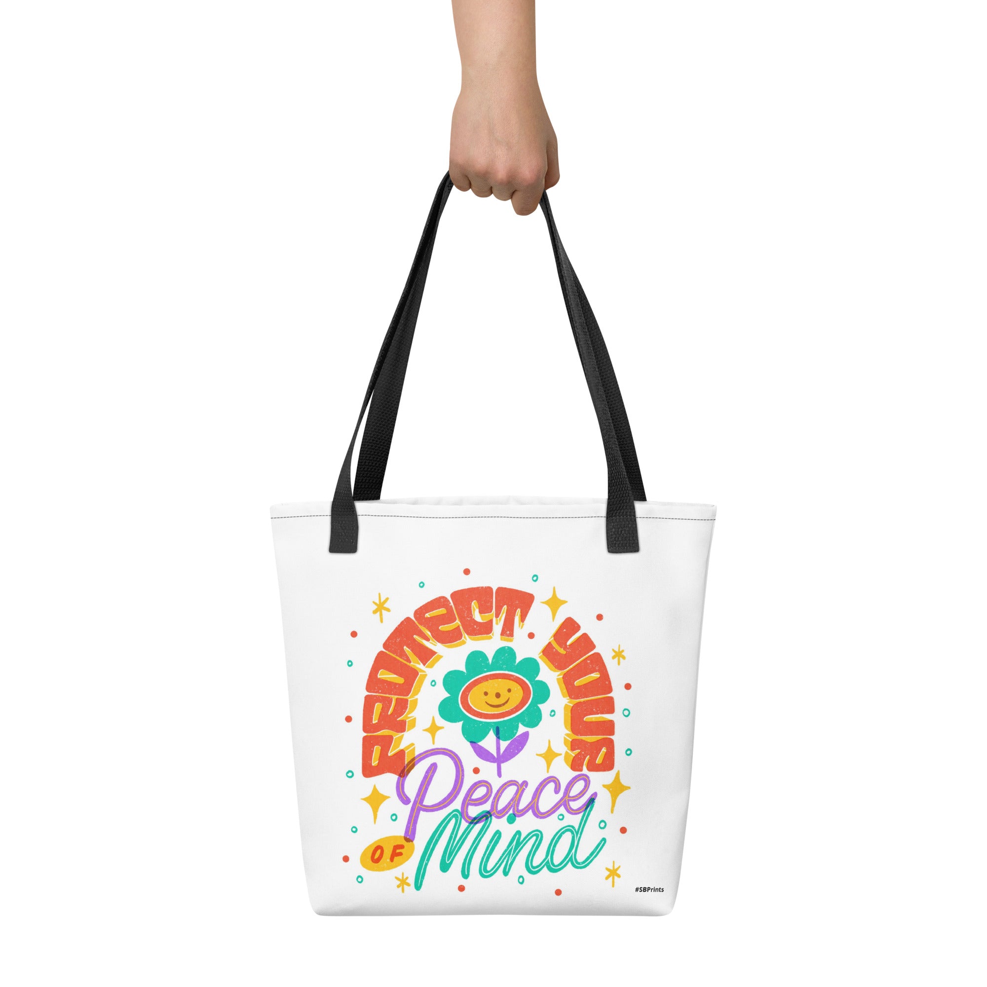 Tote bag with colorful design and text held by a hand on a white background