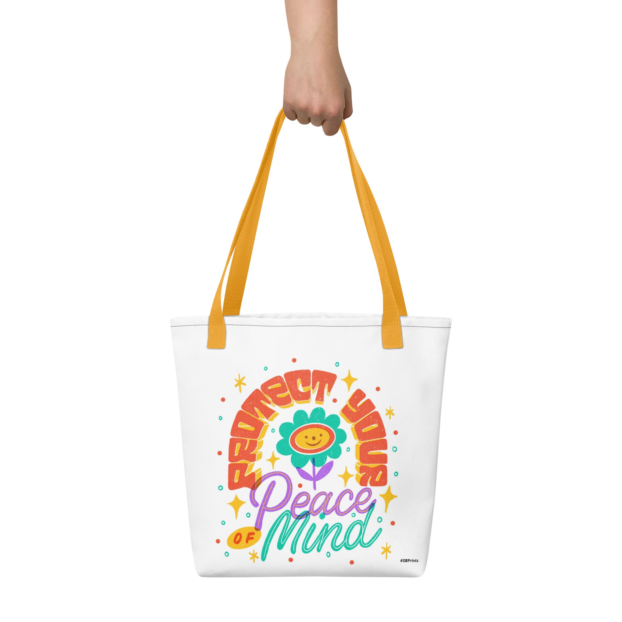 Tote bag with colorful design and text held by a hand on a white background