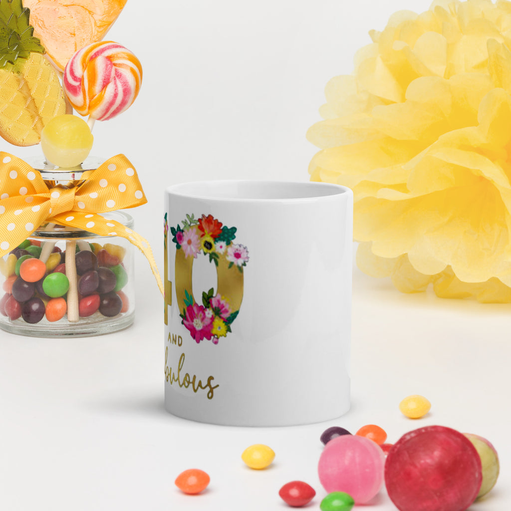 White mug with floral design and text, surrounded by colorful candies and flowers on a light background
