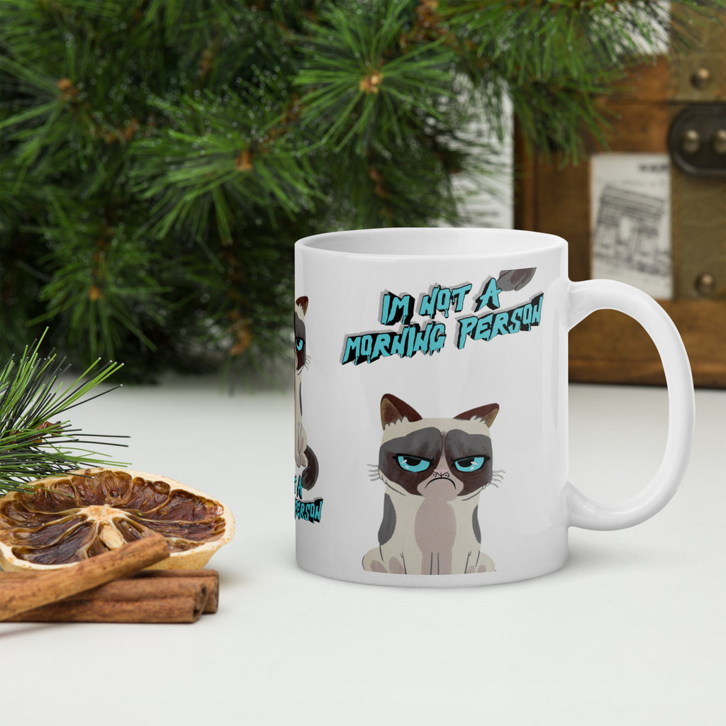 Mug with a cat illustration and text 'I'm not a morning person' on a table with decorative items.