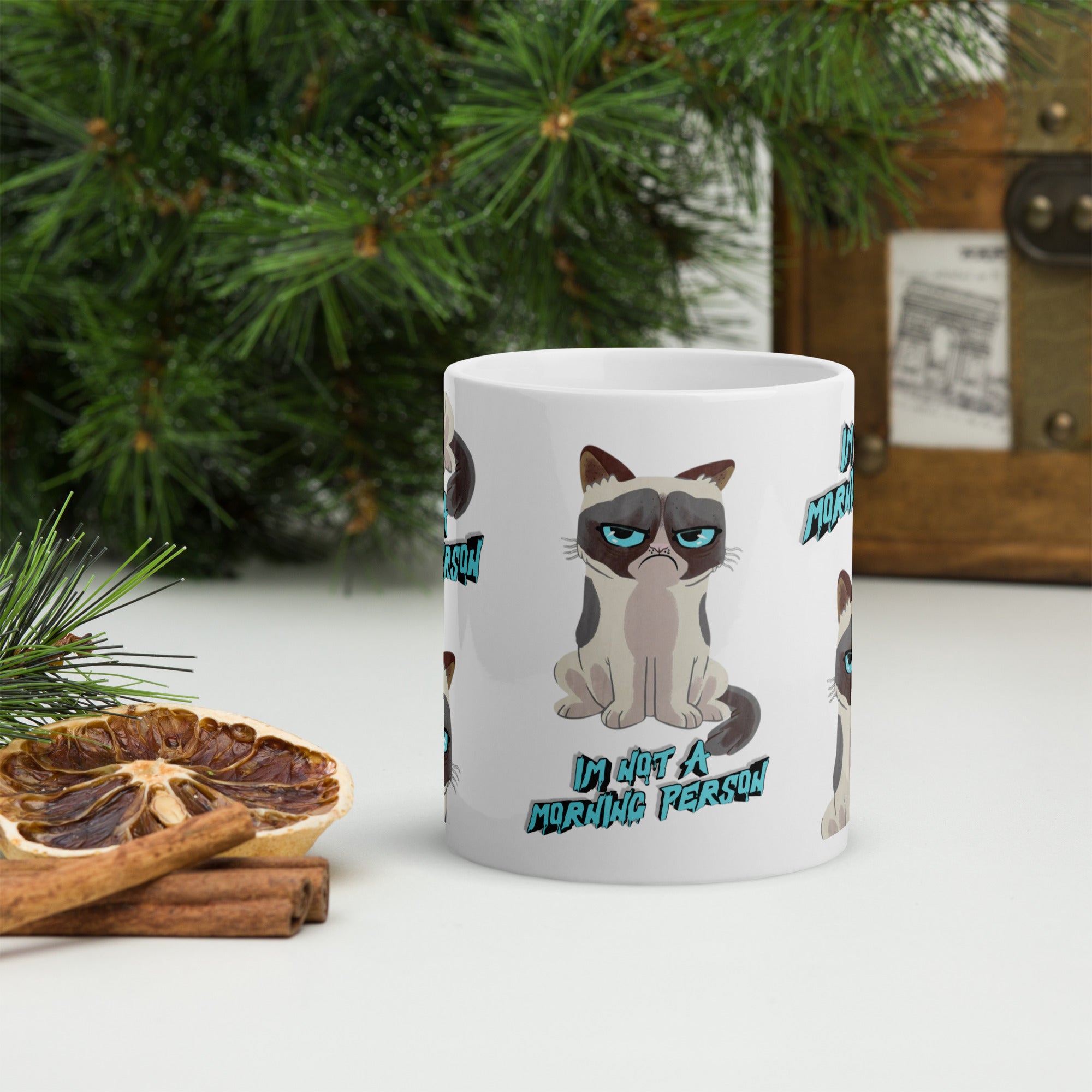 White mug with a cat design and text 'I'm not a morning person' on a surface with decorative elements.