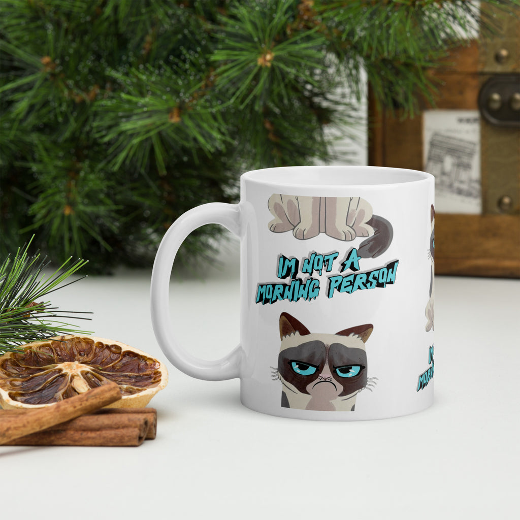 Mug with cat design and text 'I'm not a morning person' on a table with decorative items.