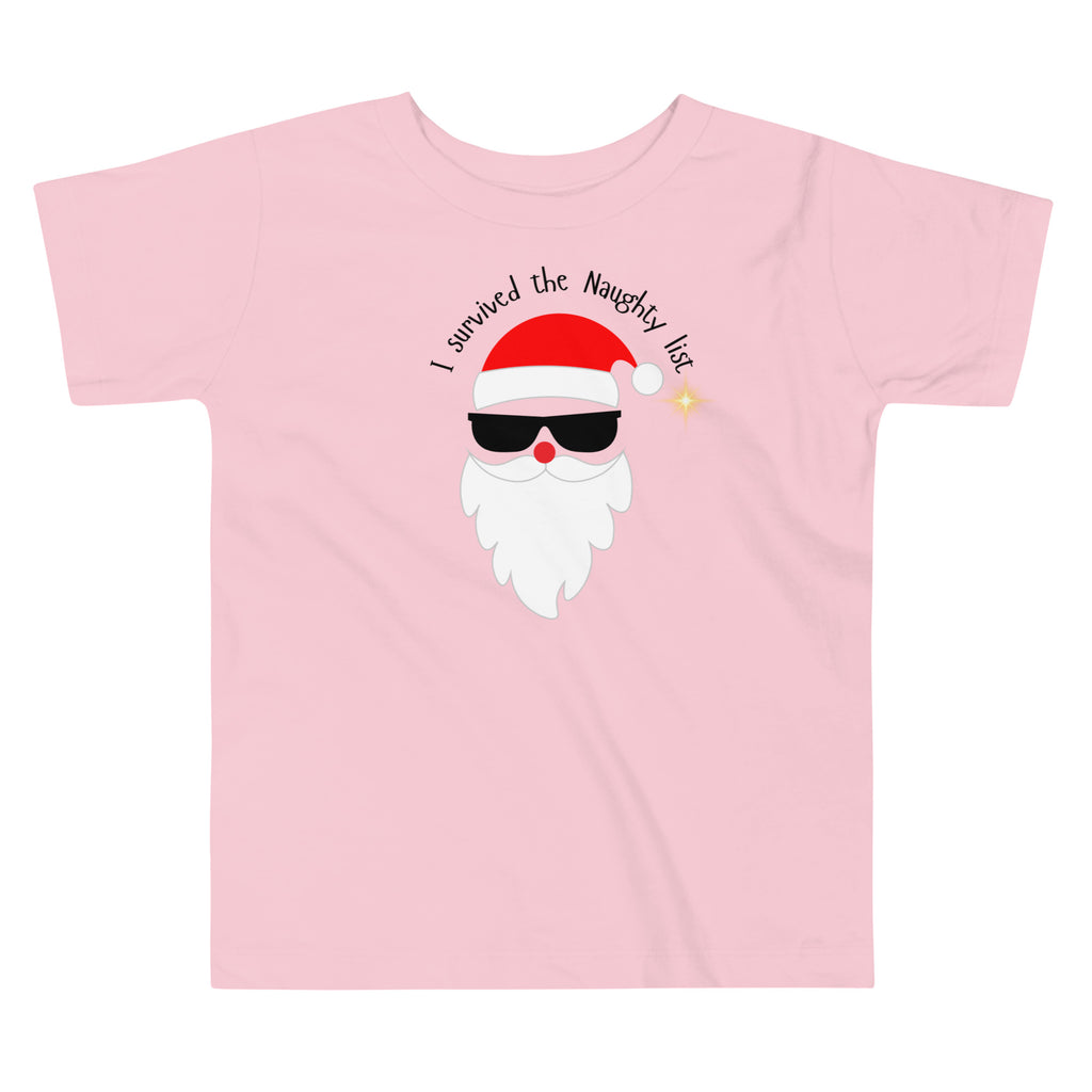 Pink t-shirt with a cartoon Santa Claus face wearing sunglasses and text 'I survived the Naughty list' on a white background.