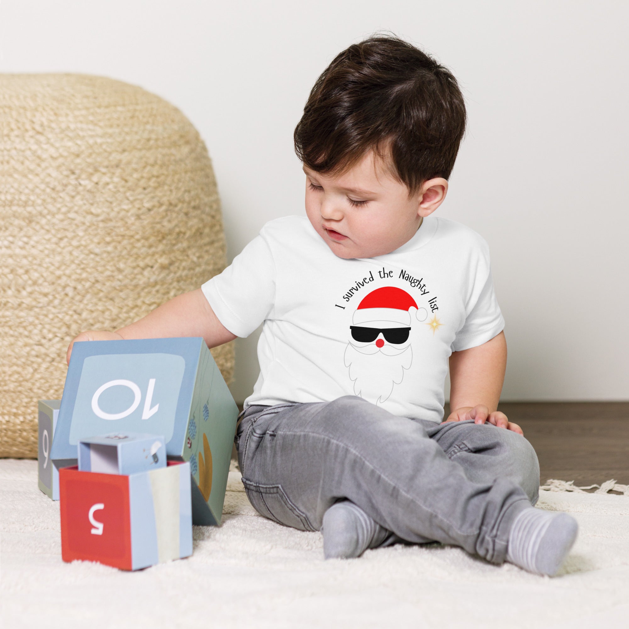 Child wearing a white t-shirt with Santa face, sitting on a carpeted floor.