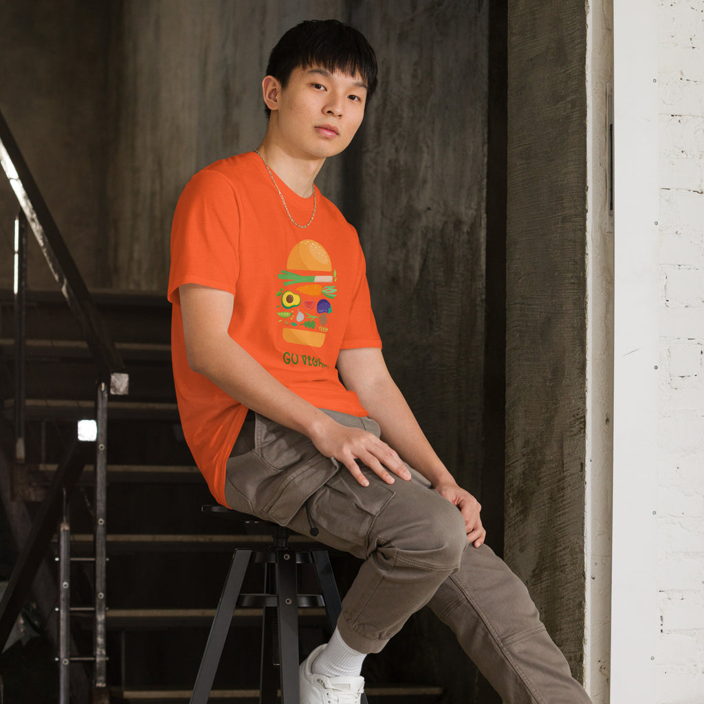 Person wearing an orange t-shirt with a graphic design, sitting on a stool in an urban setting.