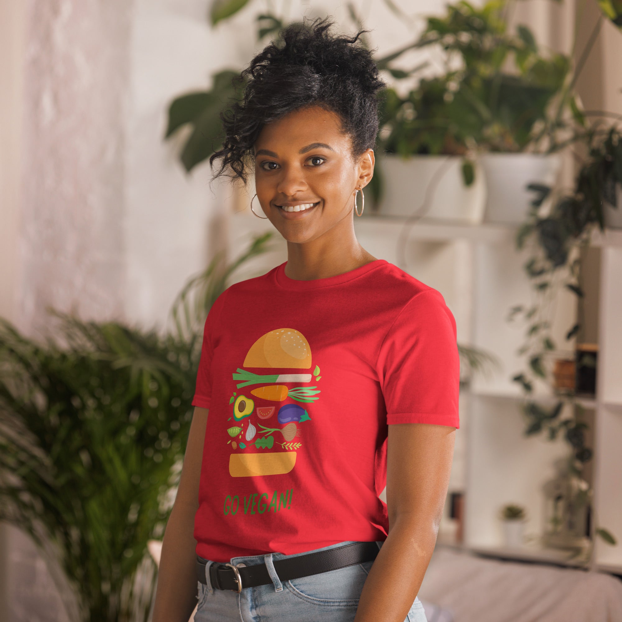 Person wearing a red t-shirt with a graphic design and text, standing in a casual setting with plants.