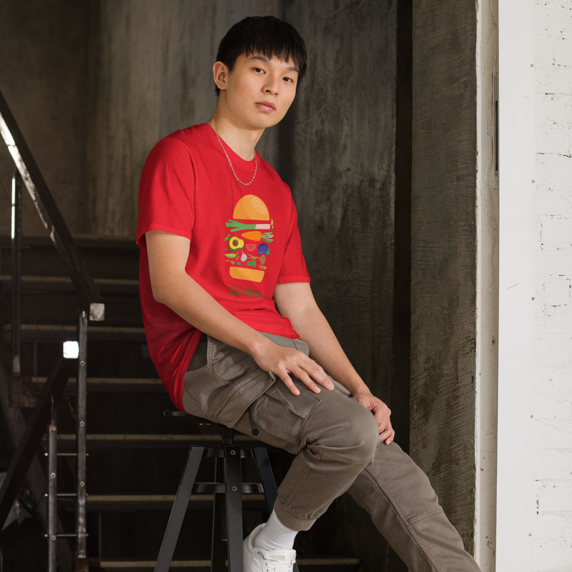 Person wearing a red t-shirt with a colorful graphic sitting on a stool in an urban setting.