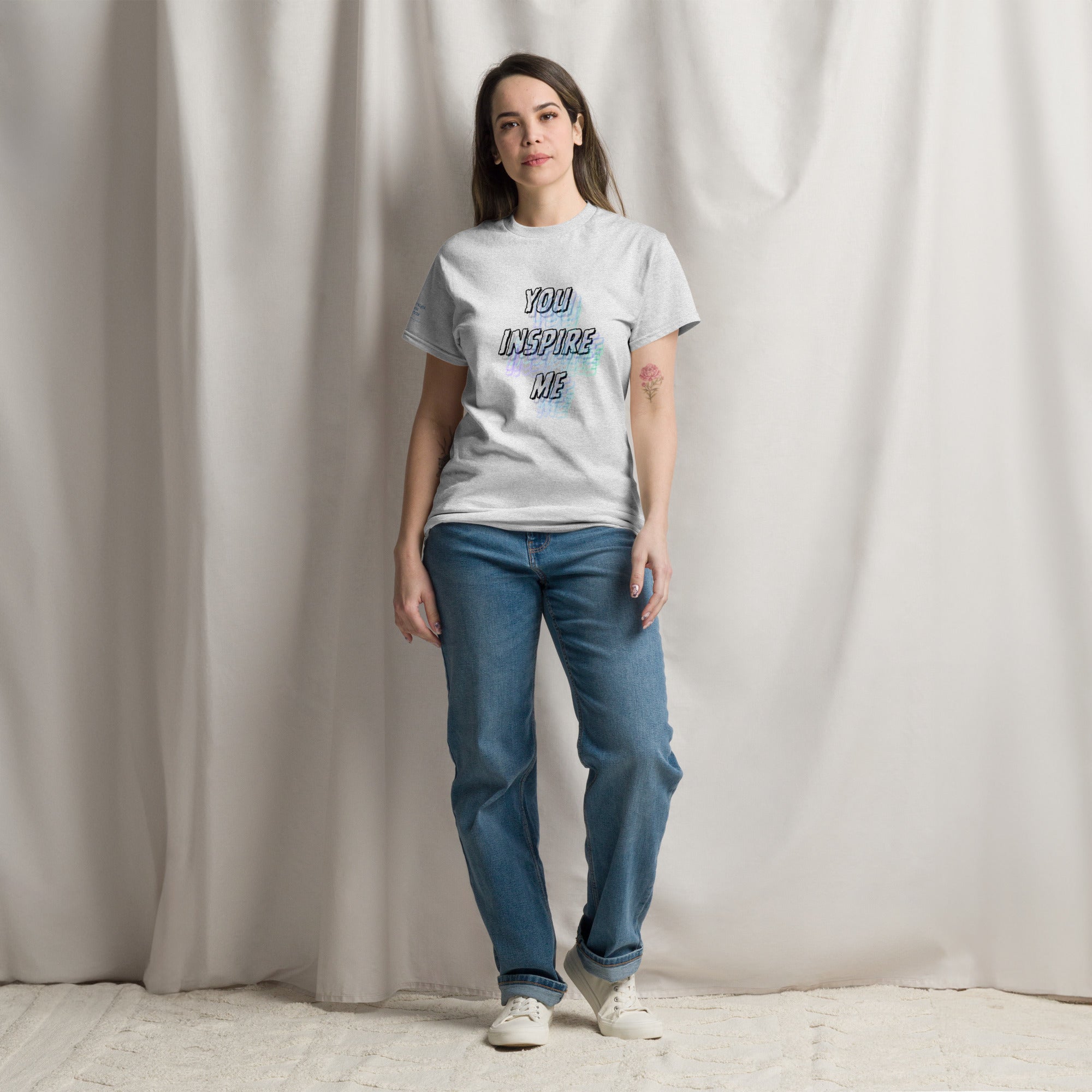 Person wearing a white t-shirt with text and blue jeans standing against a plain background