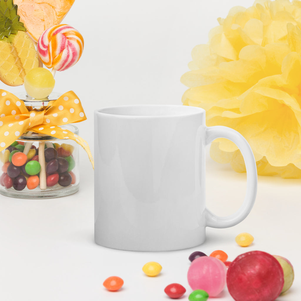 White mug on a white surface with colorful candies and a yellow flower in the background
