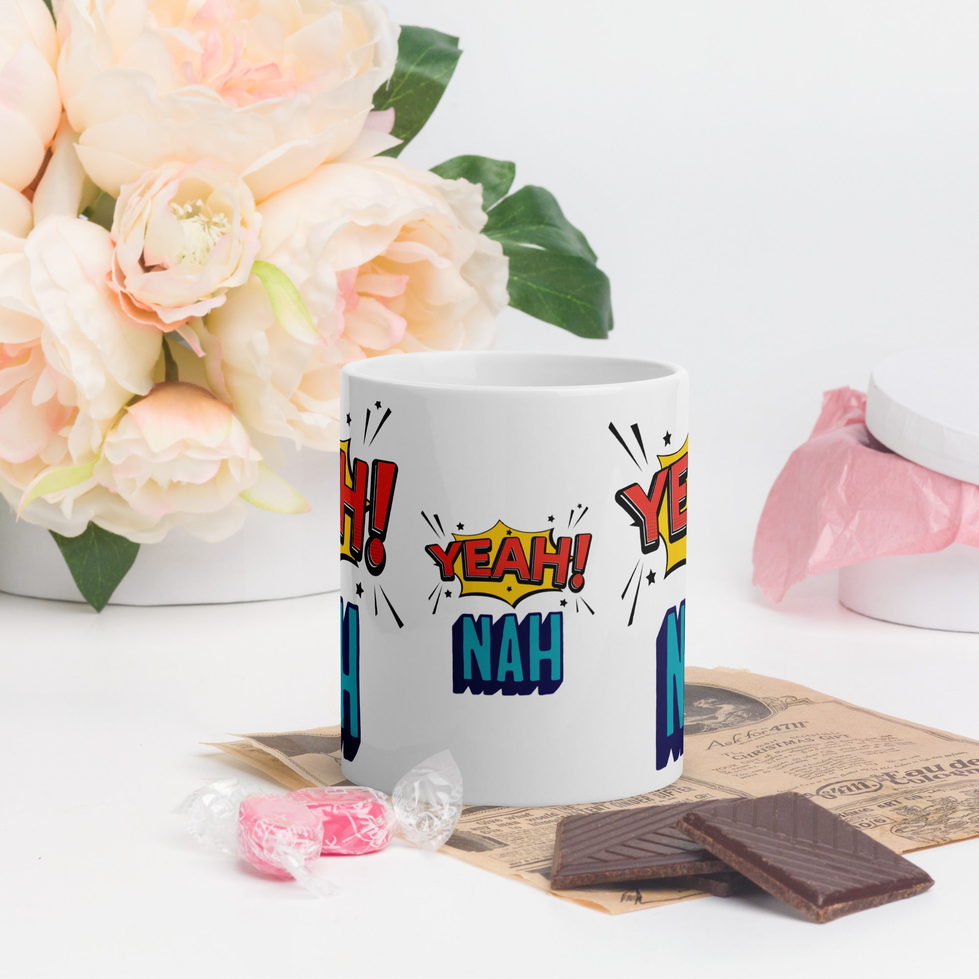 White mug with colorful text design on a table with flowers and snacks