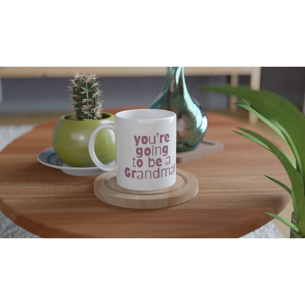 White mug with 'You're going to be a Grandma' text on a wooden table with decorative items.