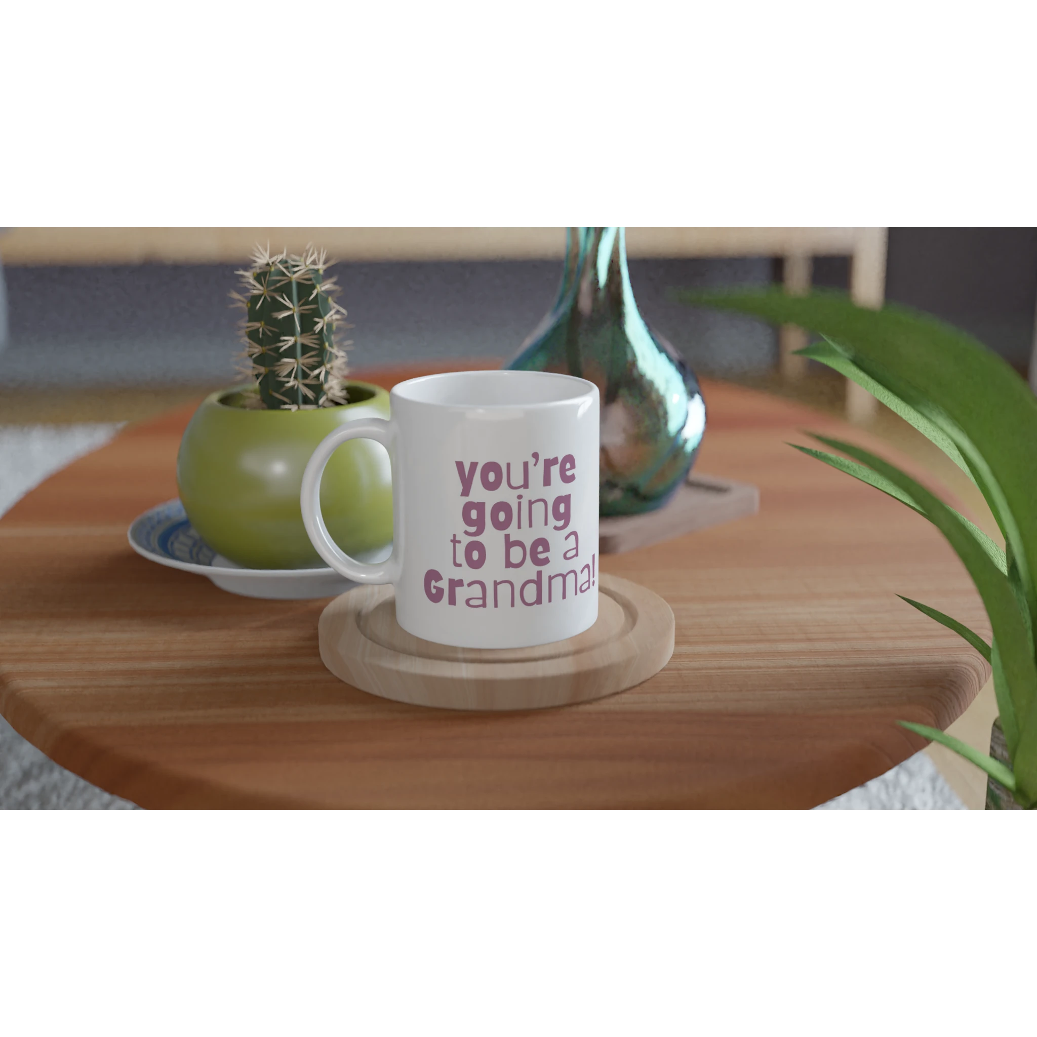 White mug with 'You're going to be a Grandma' text on a wooden table with decorative items.